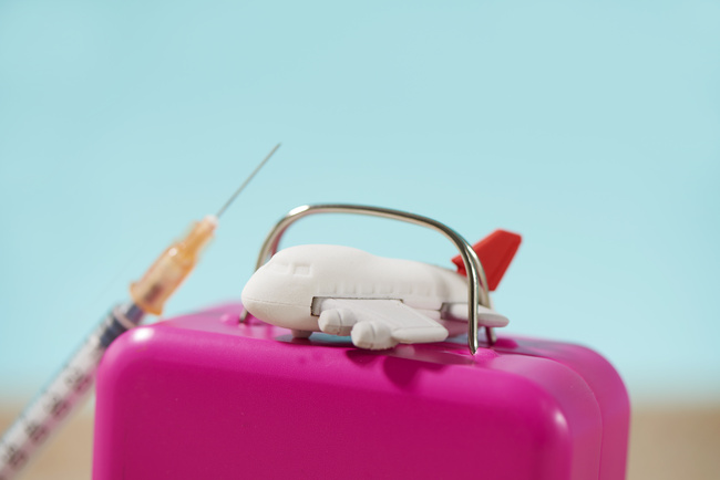 closeup of an airplane on a pink suitcase, and a syringe on the sand, on a blue background, depicting the medical tourism business