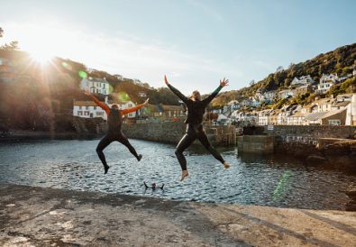 A shot of a mature woman and senior man jumping into a harbour together in wetsuits at Polperro, Cornwall.