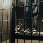 Inmate reading a book inside a prison cell while another stands nearby